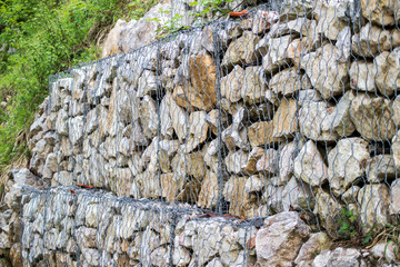 Retaining stone wall next to the road.Steel mesh of gabion wall. - 270487991