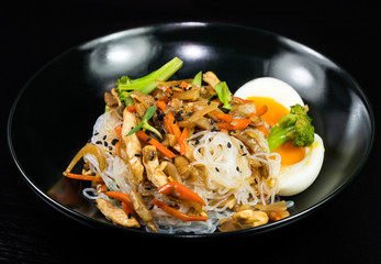 Asian noodles with vegetables and meat on a black background.