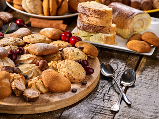 Naklejka premium Oatmeal cookies and sand chocolate cake with cherry berry and crispy wafer rolls with cream on cutting board on wooden table in rustic style. Still life served with dessert spoons. Traditional dish.