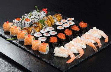 Japanese traditional rolls with seafood and fish, vegetables, on a black background.