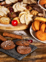 Oatmeal and nut cookies and sand biscuit on tier cake stand, crispy wafer rolls with cream on kitchen on wooden table in rustic natural style. Breakfast for loved one.