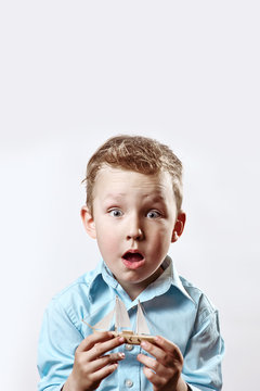 a surprised boy in a blue shirt holding a boat in his hands on a light background
