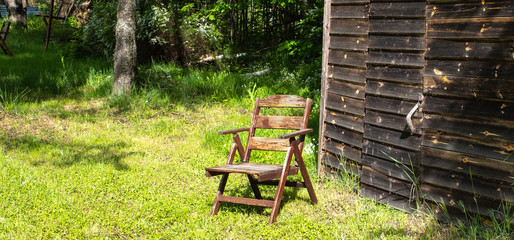Retro brown chair stands on the background of an old wooden barn, summer day and the sun's rays. Panoramic photo. Copy space