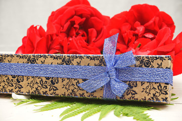 Goldene Geschenkbox mit Rosen im Hintergrund