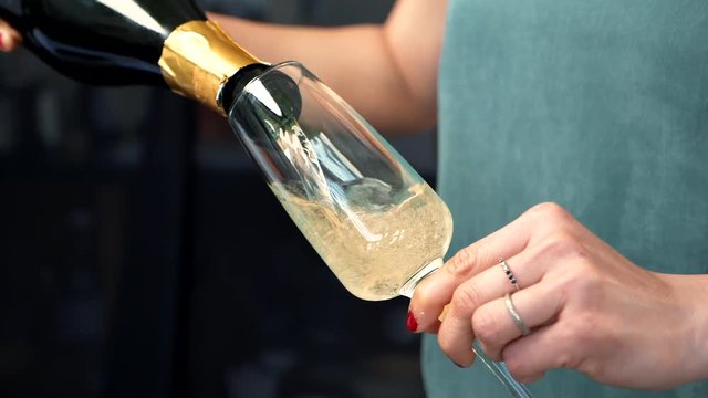 Anonymous woman hands pouring champagne in to glass with bubbles filling flute