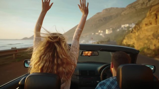 Couple on road trip with convertible driving along coast at sunset
