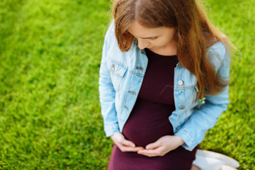 Happy young pregnant woman sitting in the park on the lawn,