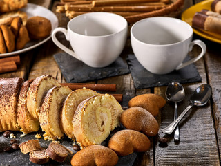 Sand cookies heart shape, rolled cake with cherry and cinnamon stick, coffee cups on kitchen on wooden table in village style. Useful for digestion. Problems with excess weight.