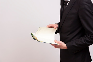 A young man in a black jacket, white shirt and black tie turns the pages of a notebook