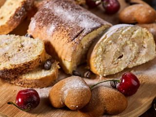 Rolled biscuit and sand chocolate cookies on board. Cinnamon stick and cherry on kitchen wood table in rustic style. Sunlight in kitchen.