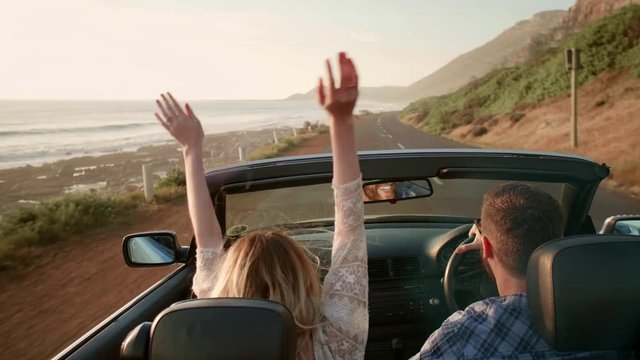 Honeymoon couple driving along the ocean in convertible at sunset