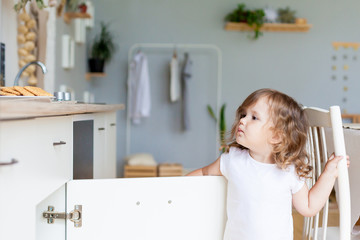 little girl opens the cupboard and tries to find something sweet in the kitchen cupboard
