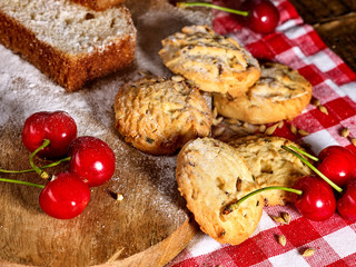 Oatmeal cookies with husk oats and cherry cupcake with powdered sugar on kitchen cutting board gingham checkered cotton fabric on table in village style for picnic. Delicious, homemade cupcake.