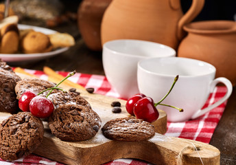 Oatmeal chocolate cookies with coffee grains and cherry, powdered sugar on kitchen cutting board with checkered fabric on wooden table in village style for picnic. Breakfast for loved one.