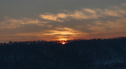Sun is setting down, lowering behind trees. Sunset over forest.