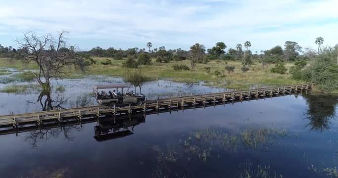 Aerial view of a safari vehicle crossing water on a pole bridge in the Okavango Delta