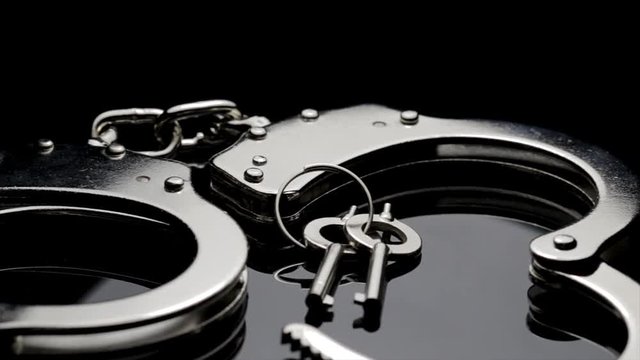 Panoramic macro view of police handcuffs and key. Shiny chrome handcuffs isolated on black background. Prisoner restraints used to lock up wrists. 