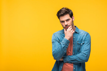 handsome pensive man touching chin Isolated On yellow