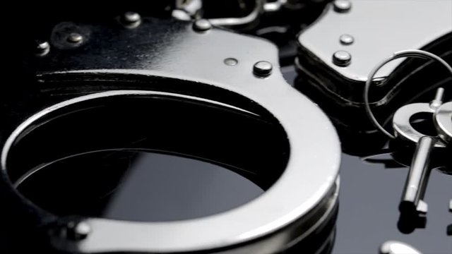 Panoramic macro view of police handcuffs and key. Shiny chrome handcuffs isolated on black background. Prisoner restraints used to lock up wrists. 