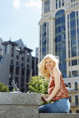 Pretty smile woman using modern laptop writing article and drink coffee near city buildings