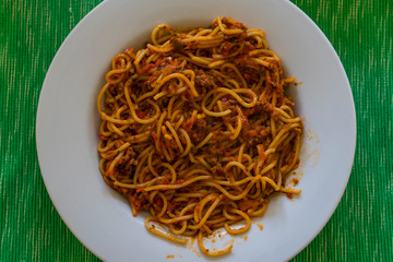 House made pasta on white plate. Pasta with meat close up. Plate sanding on a green table mat background.