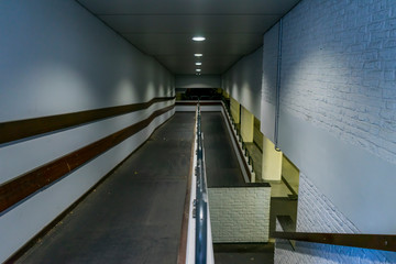 Fototapeta premium Empty walkway down to parking garage. White lamps, white walls and bricks. Stairs down.