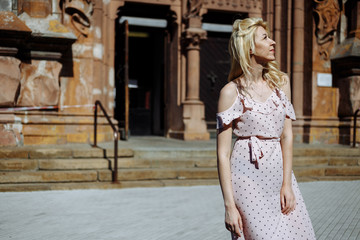 Smiling blonde woman-tourist in rose dress and white sneakers near old historical building