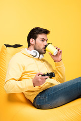 Fototapeta premium man drinking coffee to go on bean bag chair and playing Video Game Isolated On yellow