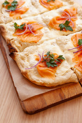 Roman pizza with smoked salmon cut in pieces and served on a wooden board