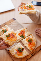 Two people eating roman pizza with smoked salmon cut in pieces and served on a wooden board