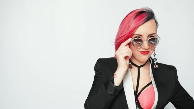 Young beautiful playful woman with pink hair looks over her sunglasses.