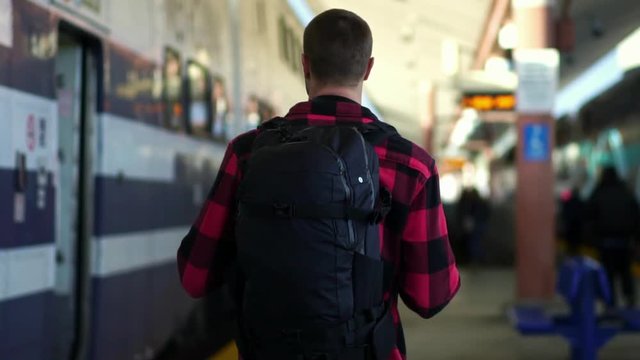 Confident backpacker guy walks by train at Los Angeles Union station. Concept of millennial on summer vacation, travel adventure, urban lifestyle.
