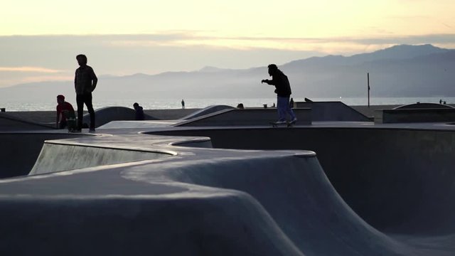 Slow Motion: Skateboarder silhouette skateboarding trick in Venice Beach skate park at sunset. Concept of Los Angeles urban lifestyle, LA tourism travel destination. 
