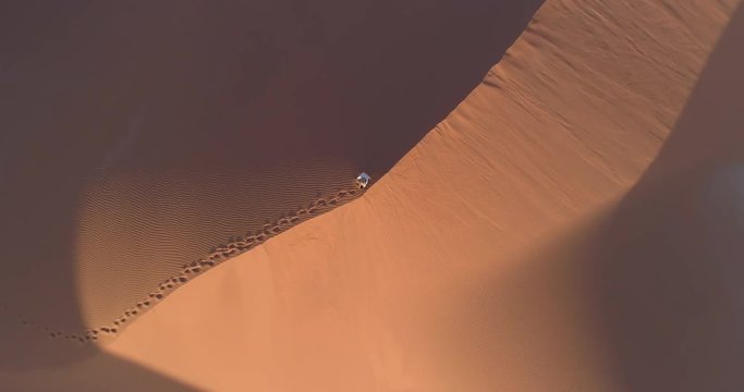 Spectacular aerial view straight up shot of tourist alone ontop of a vast sand dune in the Namib desert