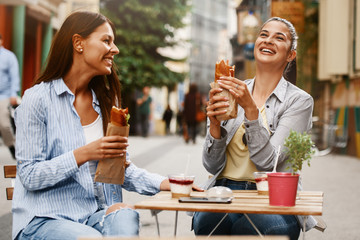 Two Female Friends Having Good Time Outdoors Eating Sandwiches