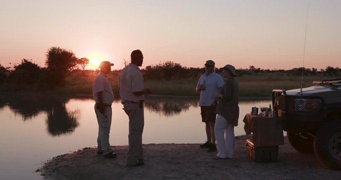 Tourists and guides enjoying a sundowner at the rivers edge in the Okavango Delta at sunset