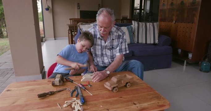 Grandfather and grandson doing some woodwork outside on a small table