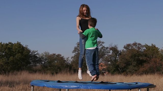 Slow motion of teenage girl and cute young boy having fun jumping on trampoline