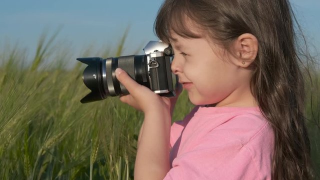 A child with a camera. A cute little girl is taking pictures in a wheat field.