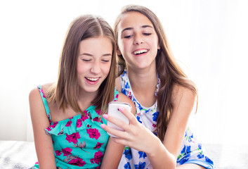 Two girls looking at smart phone, checking pictures on social media, smiling.