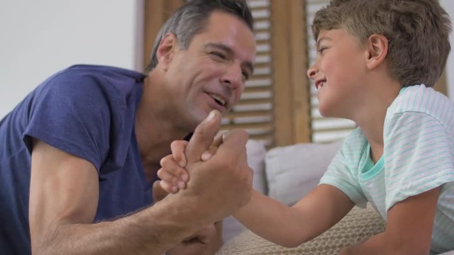 father and son arm wrestling on couch in living room 