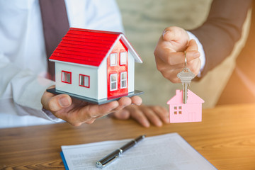 Real estate agent holding house model and keys,  customer signing contract to buy house, insurance or loan real estate.