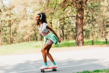 full length view of african american girl skateboarding and listening music in headphones