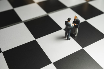 Businessman miniature handshake on chessboard background. Partnership concept.