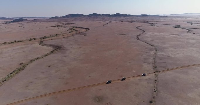 4K high aerial panning view of 4x4 vehicles driving through the Namib desert, Namibia