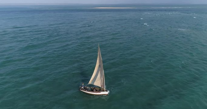 Aerial zoom out view of fisherman on a traditional dhow fishing boat heading out to sea for the days fishing