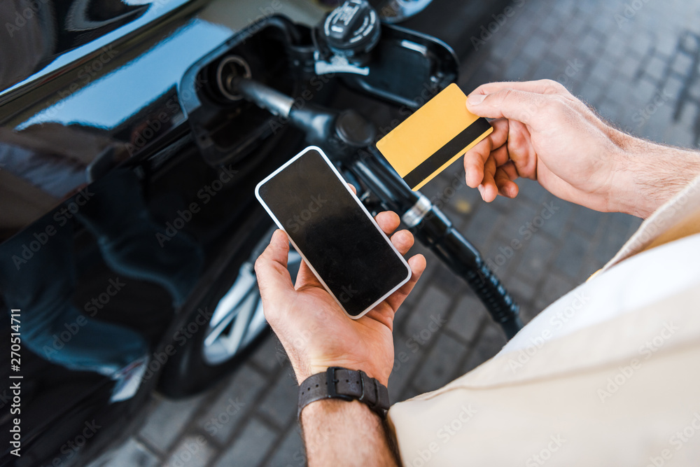 Wall mural cropped view of man holding credit card near smartphone with blank screen