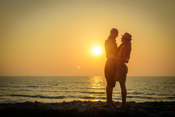 Stylish loving couple hugging each other on the beach at sunset. Man and woman in holiday honeymoon trip.