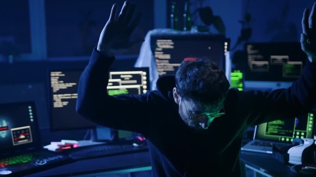 Dangerous computer hacker caught in the act of cyber crime in the company office at night. Portrait of baffled hacker raising hands to surrender to the police.