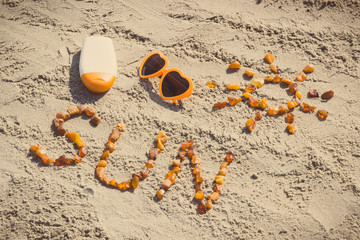 Obraz premium Vintage photo, Word and shape of sun, sunglasses with sun lotion on sand at beach